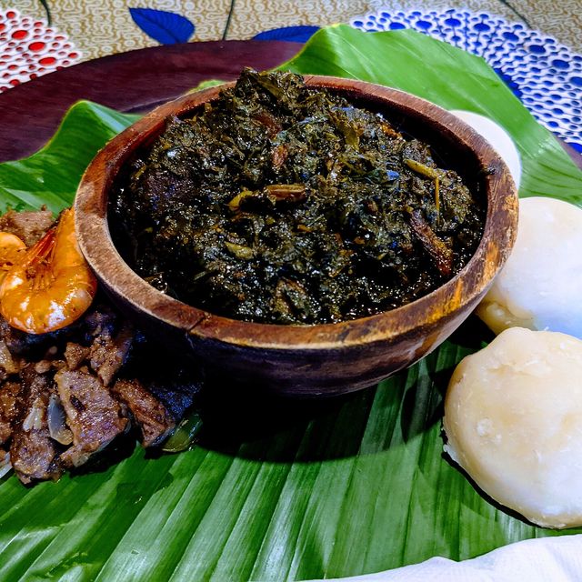 Un plat d'eru accompagné de water fufu et de viande, présenté sur une feuille de bananier