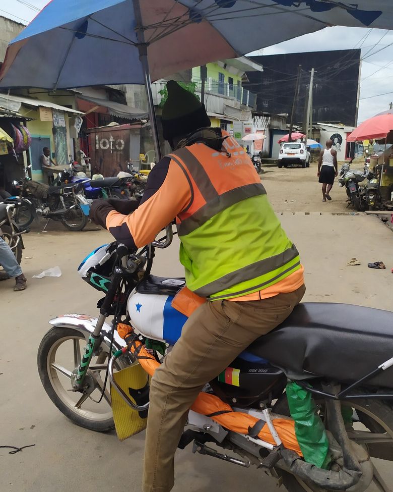 Un conducteur de moto en gilet de sécurité orange dans une rue de Douala